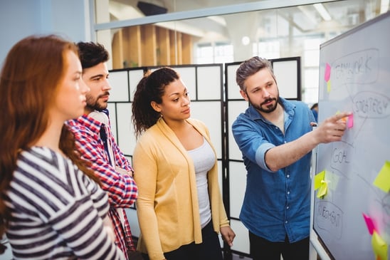 Executive explaining strategy to colleagues on whiteboard in creative office